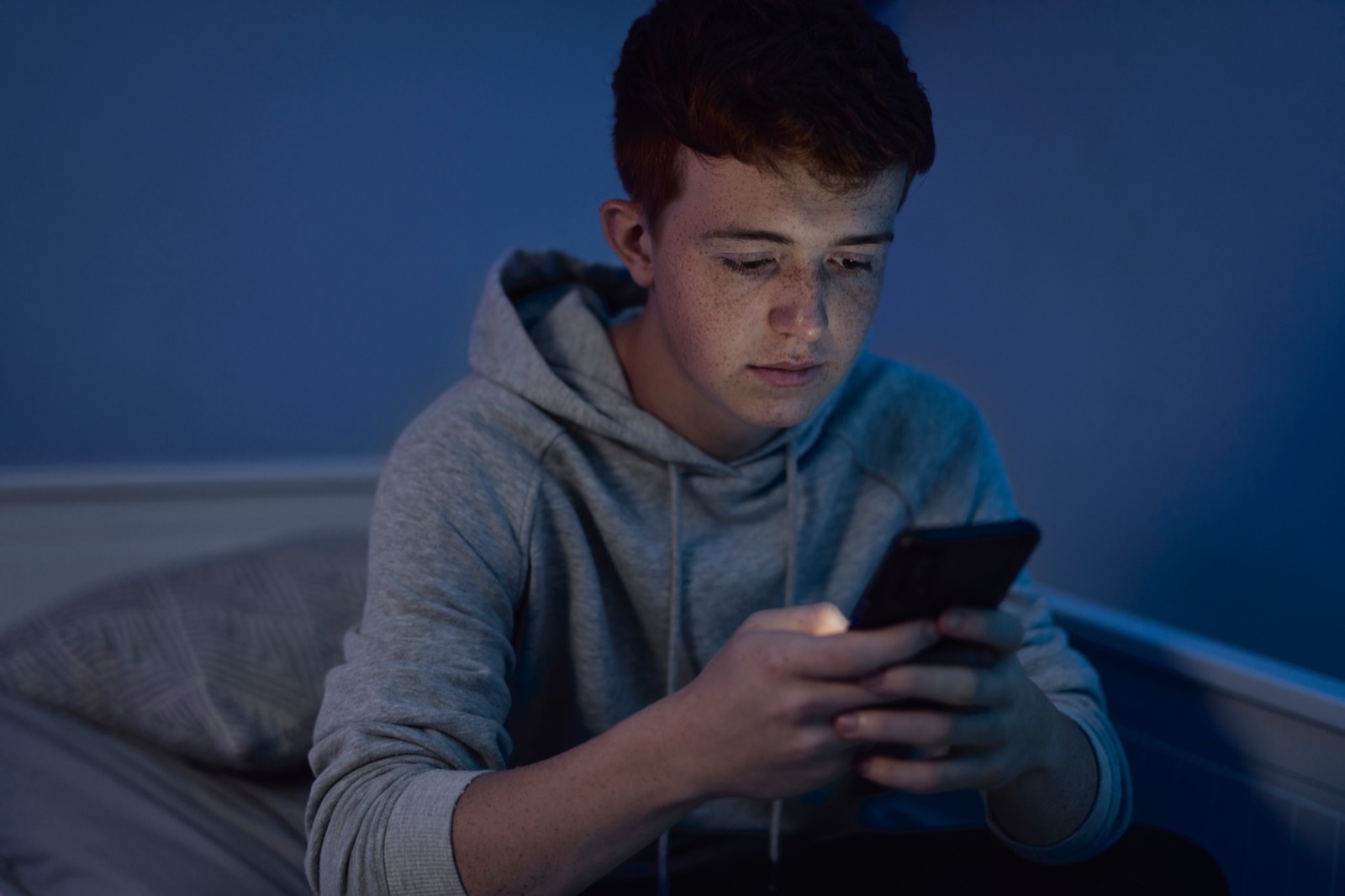 En teenagedreng sidder med sin telefon om aftenen